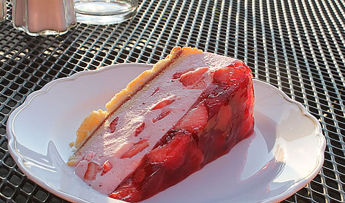 Fruchtige Erdbeertorte mit Sahnecreme und Geleeüberzug, serviert auf der sonnigen Caféterrasse des Hotel Namenlos