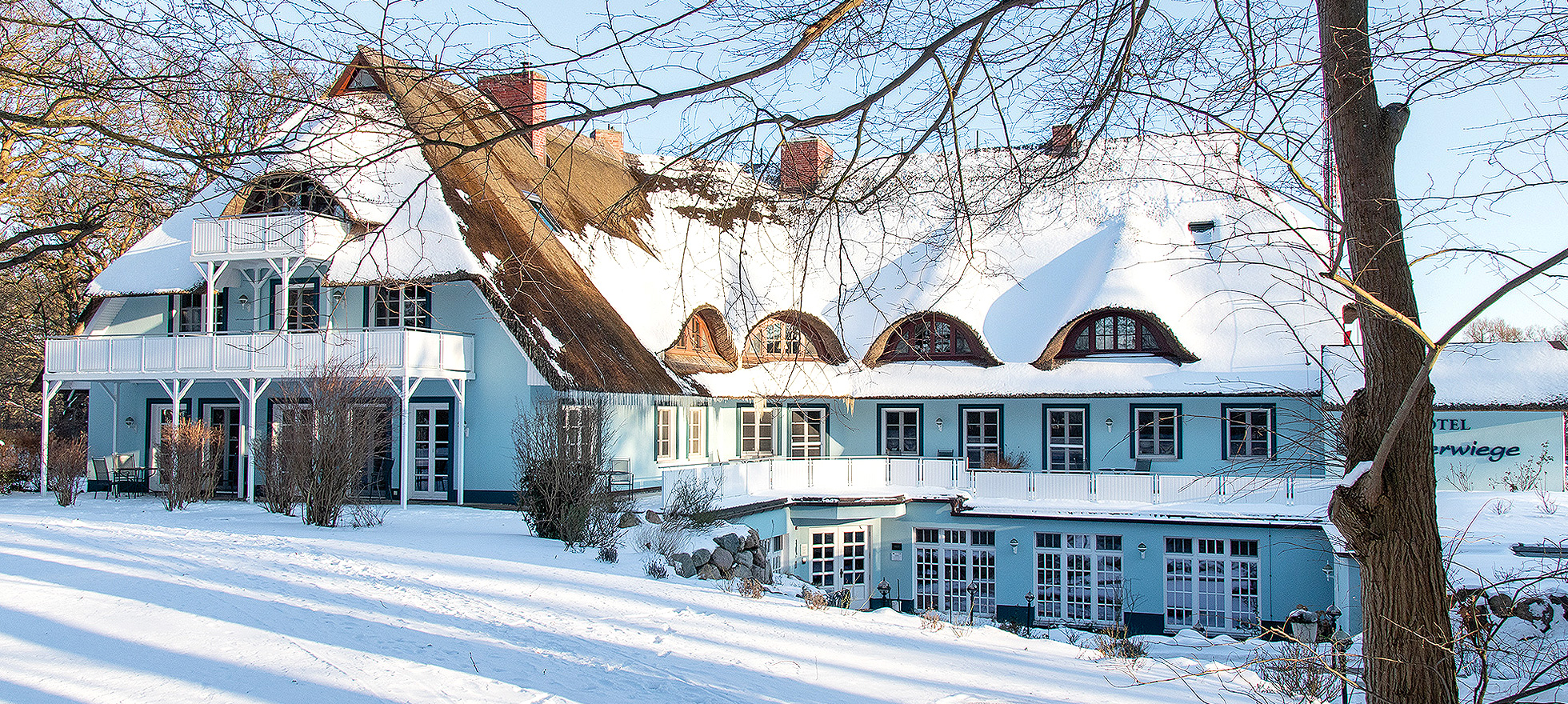 hellblaues, rohrgedecktes Hotel Fischerwiege mit viel Schnee im Winter