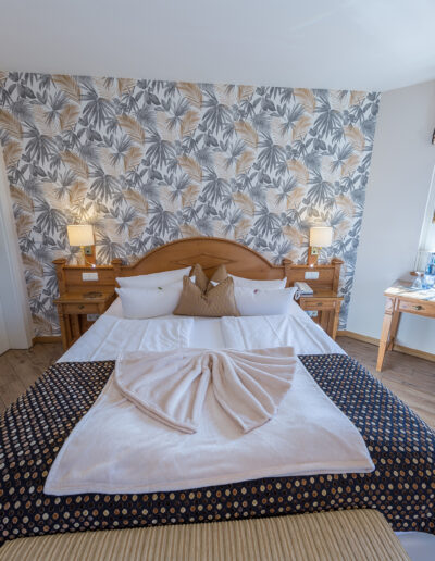 Schlafbereich in Juniorsuite, freistehendes Doppelbett, rechts kleiner Schreibtisch vor Fenster mit Blick ins Grüne