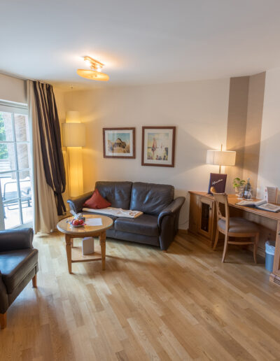Juniorsuite, links: Sitzbereich mit Zugang zum Balkon, rechts: großer Schreibtisch und Tür zum Bad