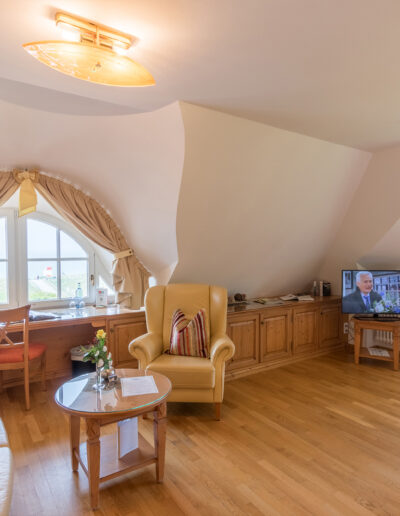 Juniorsuite, Wohnbereich, helle Sitzecke und Schreibtisch vor Rundbogenfenster mit Blick auf Ostsee