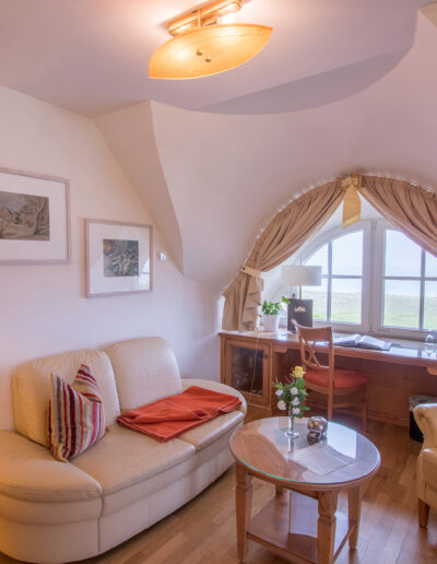 Juniorsuite, helle Sitzecke und Schreibtisch vor Rundbogenfenster mit Blick auf Ostsee