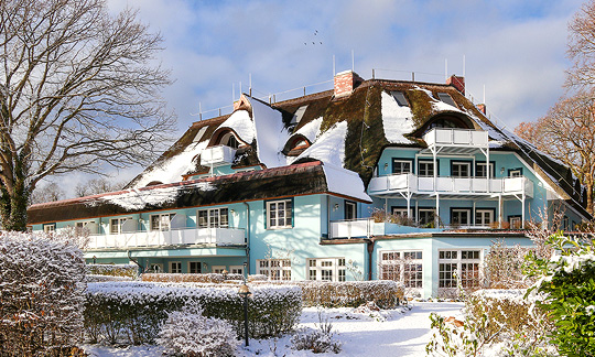 Romantik Hotel Fischerwiege im Winter Reetgedecktes, hellblaues Haus mit Rundbogenfenstern und verschneitem Garten, Romantik Hotel Fischerwiege