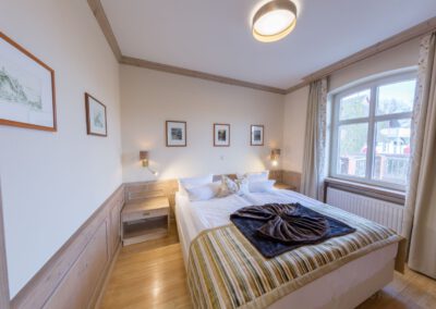Schlafzimmer mit Doppelbett, zwei Nachttischen und großem Fenster mit Blick auf Balkon und Reetdachhaus