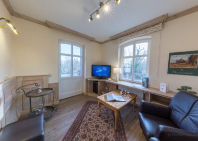 Wohnbereich mit zwei Ledersesseln, Holztisch, Fernseher und großem Fenster mit Blick ins Grüne